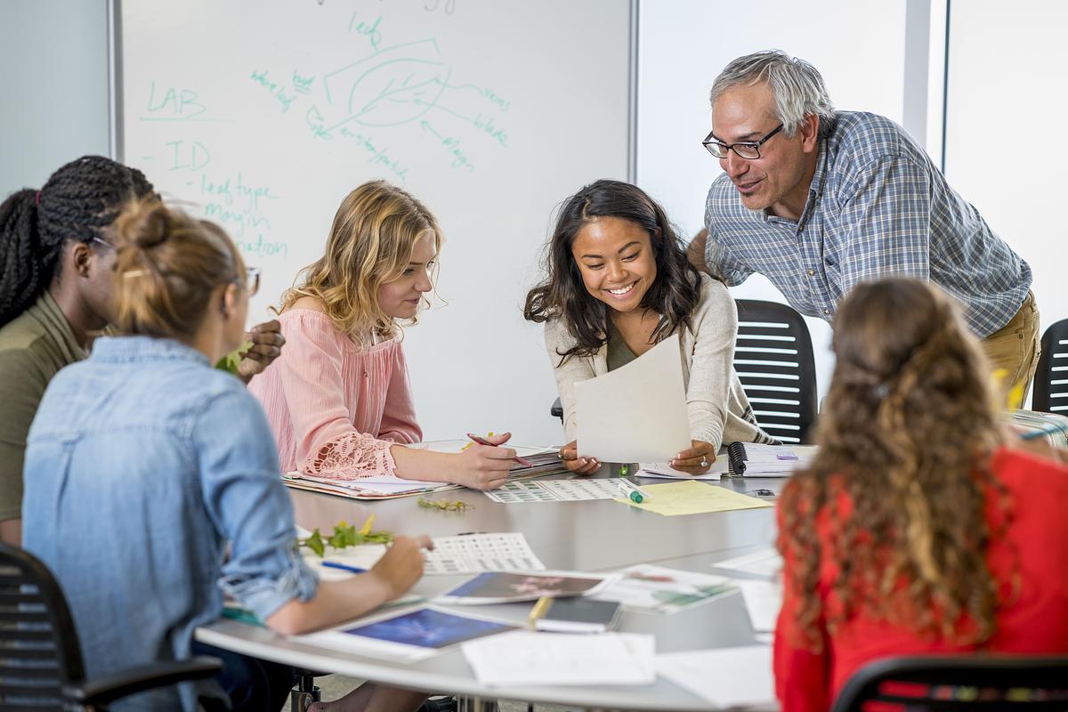 A group of students collaborate at a desk with their professor.