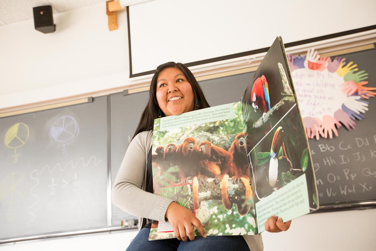 A teacher pointing to parts of a large book on Biology in front of the classroom.